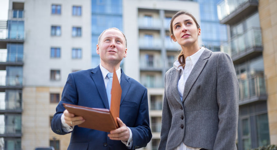 A man holding a clipboard with a woman surrounded by apartment buildings