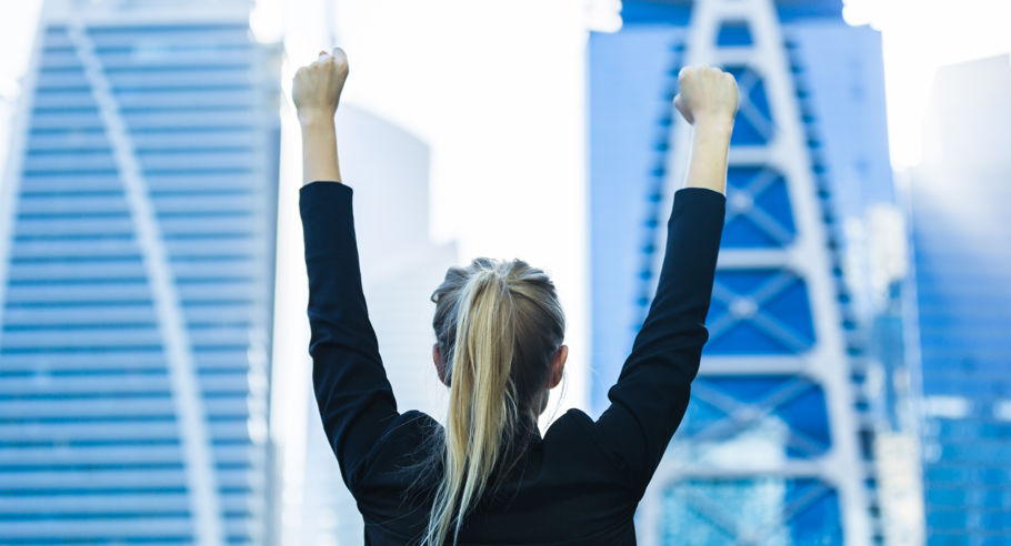 A behind shot of a woman with her hands up in celebration with a backdrop of a city skyline