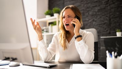 A woman sitting with a laptop on the phone looking frustrated