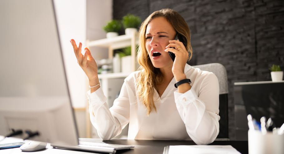 A woman sitting with a laptop on the phone looking frustrated