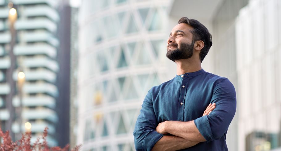 A man looking happy with his arms crossed on a balcony surrounded by skyrises