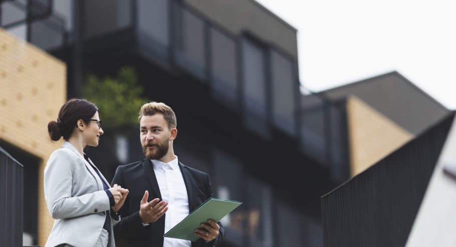 Two people in suits talking in front of an apartment building