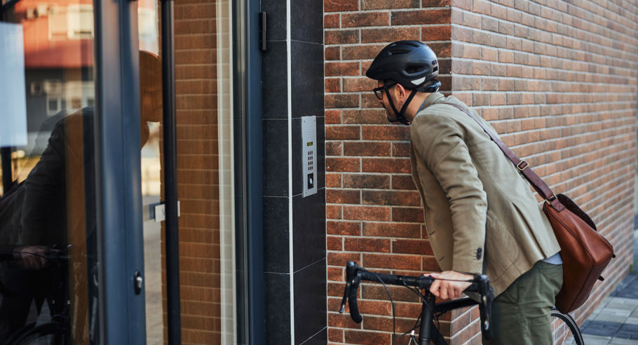 A man on a bicycle looking at a comms system outside a building